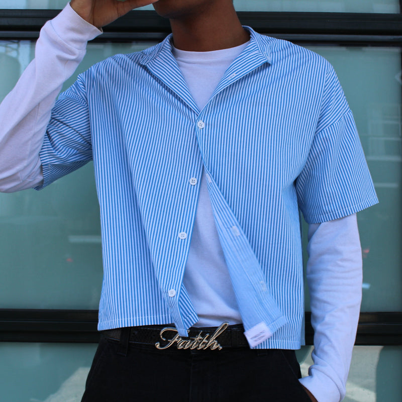 Person wearing a blue checkered shirt over a white long-sleeve shirt, standing in front of a glass door.